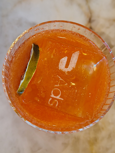 Overhead shot of a bright orange cocktail with a lime and an ice cube emblazoned with the DoorDash Ads logo.